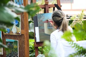 Older lady with grey ponytail painting picture in garden