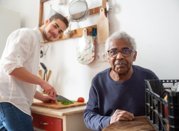 A young adult helping a senior in the kitchen, highlighting care and support at home.